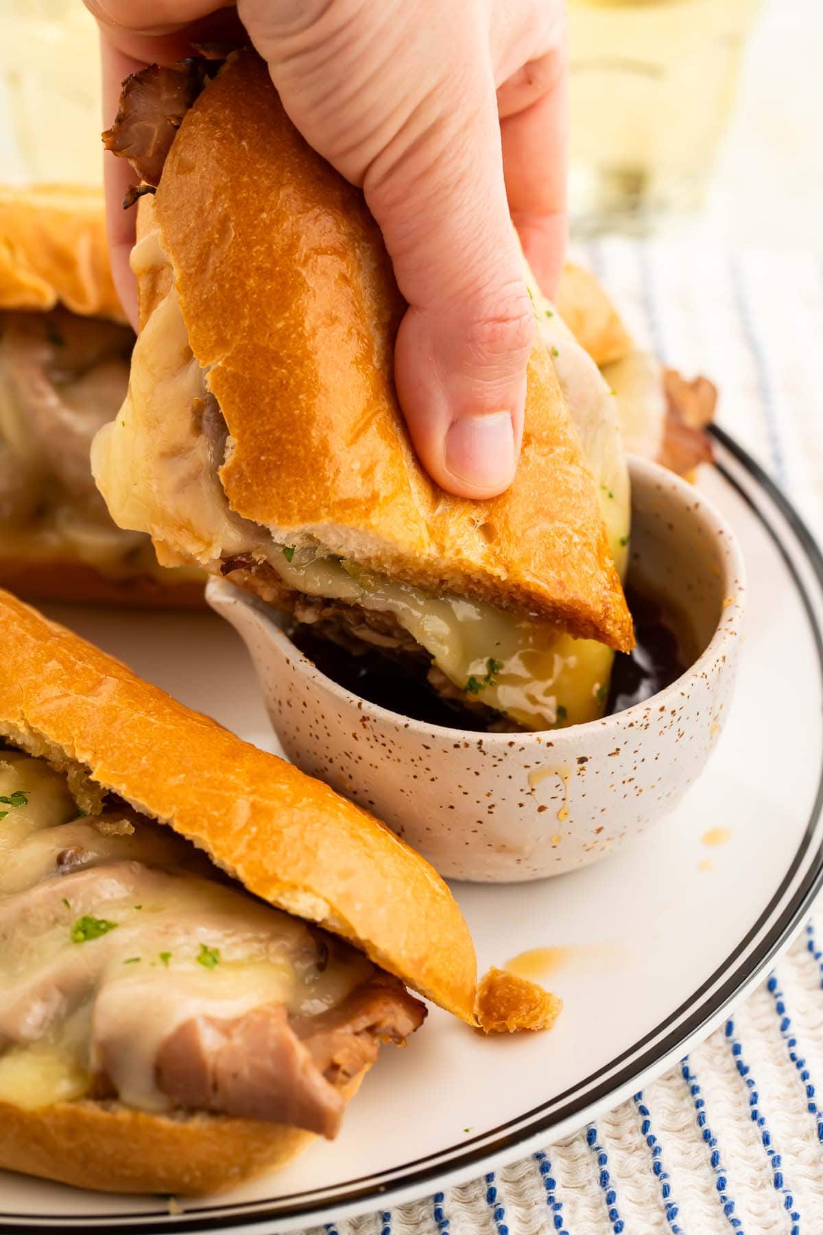 A french dip sandwich served au jus being dipped into a small bowl of jus.