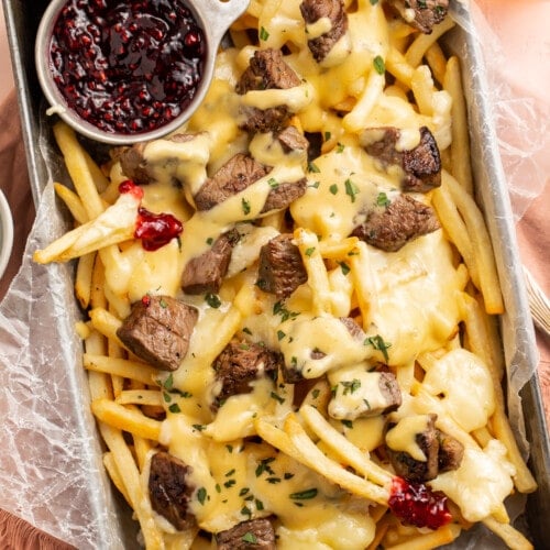Overhead, angled view of baked brie and steak cheese fries in a rectangular deep pan with raspberry preserves.