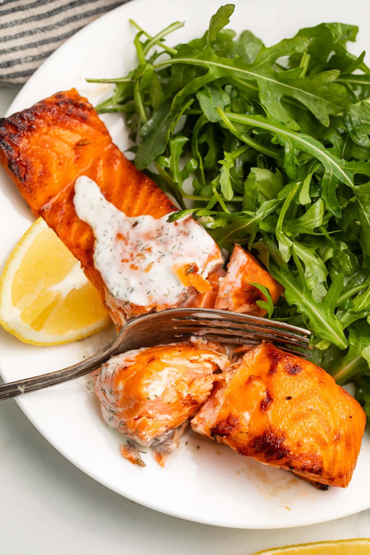 A salmon fillet, cooked in an air fryer, topped with a creamy dill sauce and served with a small salad.