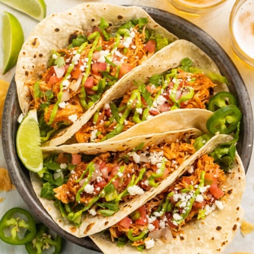 4 stuffed chicken tacos arranged on a plate. The tacos are filled with lettuce, tomato, cheese, and shredded chicken.