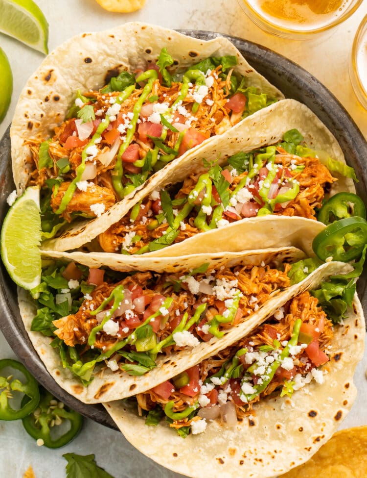 4 stuffed chicken tacos arranged on a plate. The tacos are filled with lettuce, tomato, cheese, and shredded chicken.