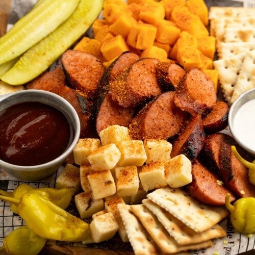 Close-up, overhead view of a Memphis-style cheese and sausage plate with pickles, crackers, ranch, and BBQ sauce on newspaper.